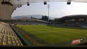 An empty football stadium on a sunny day with mountains in the background.