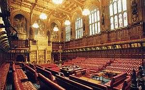 Wood panelled room with high ceiling containing comfortable red padded benches and large gold throne.