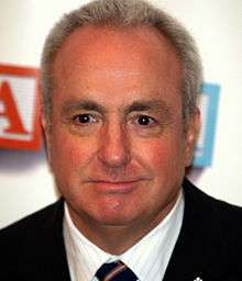 A close-up of Lorne Michaels—a middle-aged Caucasian man with white hair wearing a black suit—as he smiles