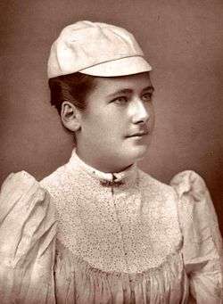 A black and white picture, a woman is in all-white attire with a hat on, and is looking sideways to the camera