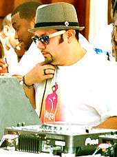 A man wearing a white T-shirt and bowler hat at a mixing table
