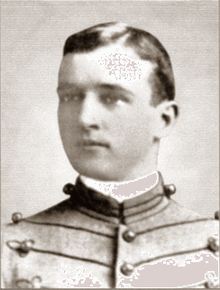 Head of a young white man with neatly combed hair wearing a jacket with lines of decorative piping running horizontally across the chest.