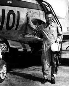 A man in a flight suit standing next to an aircraft.