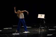 Louise Lecavalier performing in Pite's work "Lone Epic." Beside the dancer is a music stand with sheet of paper displaying "?".