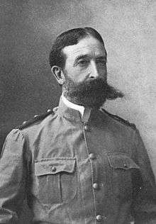 Head and torso of a white man with a close-cropped beard and a very wide, pointed mustache, wearing a military jacket with breast pockets and shoulder boards.