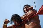 A Mexican wrestler acting like he is choking his opponent with the top rope.