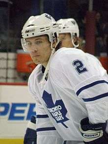 A chest up shot of a young man wearing a white hockey jersey and helmet. There is a blue maple leaf logo on the jersey, with the words 'Toronto Maple Leafs'.