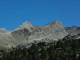 Two barren, grey granite peaks rising from a ridge, against the blue sky