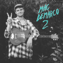 Picture of Mac DeMarco and his guitar.  He is smiling and wearing a baseball cap.
