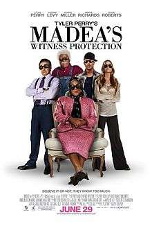 The poster shows five people, four standing and one sitting in chair wearing black sunglasses in a white background. Text at the top of the poster reveals the title. Text at the bottom of the poster reveals the production credits, rating and release date.