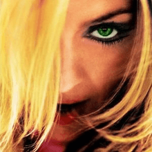 Close-up image of Madonna looking to her front and with her opened mouth. She is wearing mascara in her green eyes and her blonde hair hides part of her face.