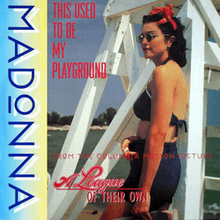 Madonna wearing sunglasses and beachwear, while standing in front of a white lifeguard tower.