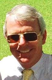 a smiling, clean-shaven middle-aged white man with grey hair, wearing sunglasses
