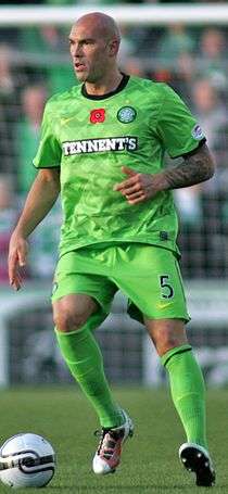 A photograph of a footballer in action on the pitch, the man is bald and he is wearing an all light green football kit, he is seen with the ball in his possession.
