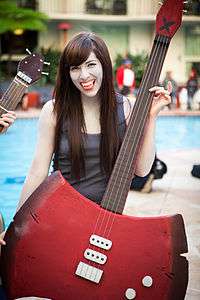 A woman, dressed in a grey shirt holding a red axe-bass hybrid.