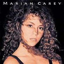 A curly-haired young brunette woman with black straps around her shoulders. The words "MARIAH CAREY" on the top of the image, upper-cased.