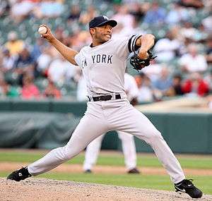 A right-handed Hispanic baseball pitcher, wearing a grey uniform with the lettering "NEW YORK" across it, with his body facing the image, in his throwing stance.