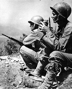 Two men in military uniforms standing on a ledge overlooking a river