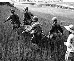 Several men carry a man on a stretcher through a field of grass