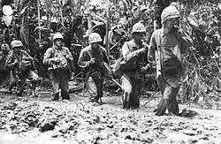 Marines standing in knee-high mud in the jungle.