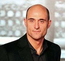 A head-and-shoulders view of a bald middle-aged Strong, wearing a dark shirt and black jacket.