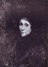 A young woman dressed in black with a black cap covering her hair