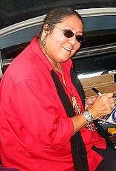 A woman wearing sunglasses and a red jacket signing a compact disc