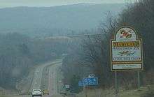 A sign adjacent to a four-lane highway reads "Maryland welcomes you. Enjoy your visit! Martin O'Malley, Governor"