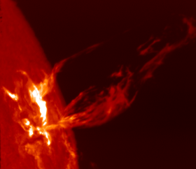 At left is a section of a red disk with an irregular bright region. Streams of red plasma trail off to the right.