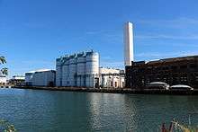 Five silos sit on a dock across the water, along with an old warehouse