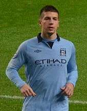 Short-haired young man on a field wearing a light-blue sports jersey.