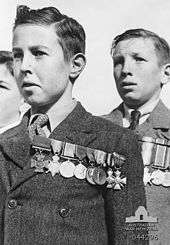 Black and white photograph of three boys. The two boys in the centre and right-hand side of the photo are wearing formal suits with medals pinned on the left-hand side of their chest. Only part of the head of the third boy is visible on the left-hand side of the photo.