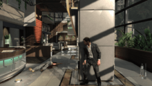 The player character positioned in cover behind a pillar, inside a building, while enemies hunt him down.