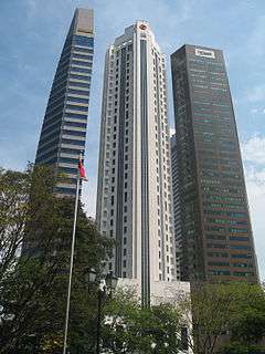 Ground-level view of three 40-storey towers. The building on the left is very thin with a blue and grey facade. The building in the center has a square cross section with diagonal, cut-off corners and a tapering roofline. The building on the right is box-like with diagonal corners and a brown facade.