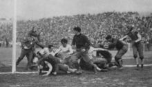 A black-and-white picture of a man observing several football players in a pile