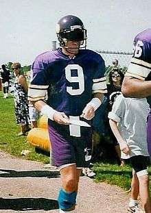 A white man wearing a purple jersey with white trim and a large numeral "9" in white on his chest. He is wearing a purple American football helmet with a dark visor covering his eyes.