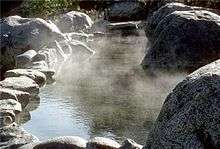 Steaming pool of water surrounded by a group of rocks.