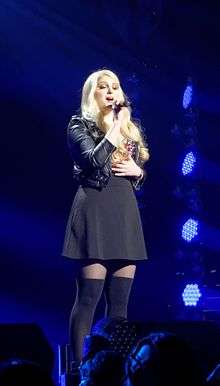 Meghan Trainor performing on stage with blue stage lighting shining upon her