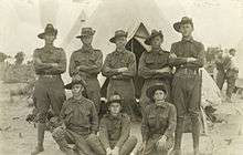 A portrait of several soldiers wearing upturned slouch hats in front of a tent during a training camp