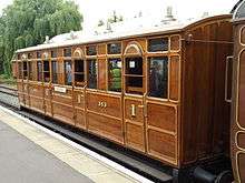 Side view of a varnished wooden railway carriage with doors and windows at regular intervals down the side.