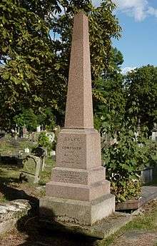 A red granite obelisk surrounded by other gravestones