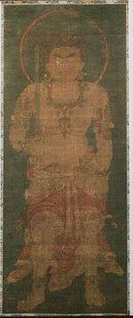 Frontal portrait of a frightening deity dressed only in a skirt-like garment holding a sword in his right hand.