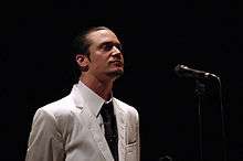 A man in a white suit standing in front of a microphone stand