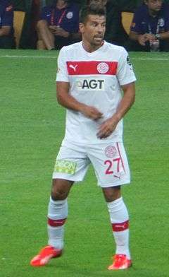 Photograph of a player in a white football kit standing on grass