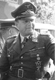 A man wearing a peaked cap and military uniform with various military decorations including an Iron Cross displayed at the front of his uniform collar.
