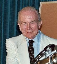 man in business suit, microphones in foreground