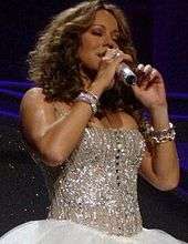 A woman smiles and holds a microphone, wearing a metallic dress.