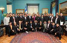 Color image ofLos 33 miners posing with the President and First Lady of Chile in the Blue Room of the Presidential Palace on 24 October 2010