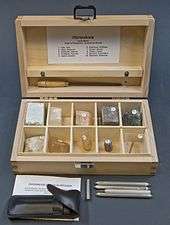 Open wooden box with ten compartments, each containing a numbered mineral specimen.