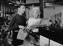 Monroe and Montand standing next to a piano in a studio-type setting and looking at sheet music.